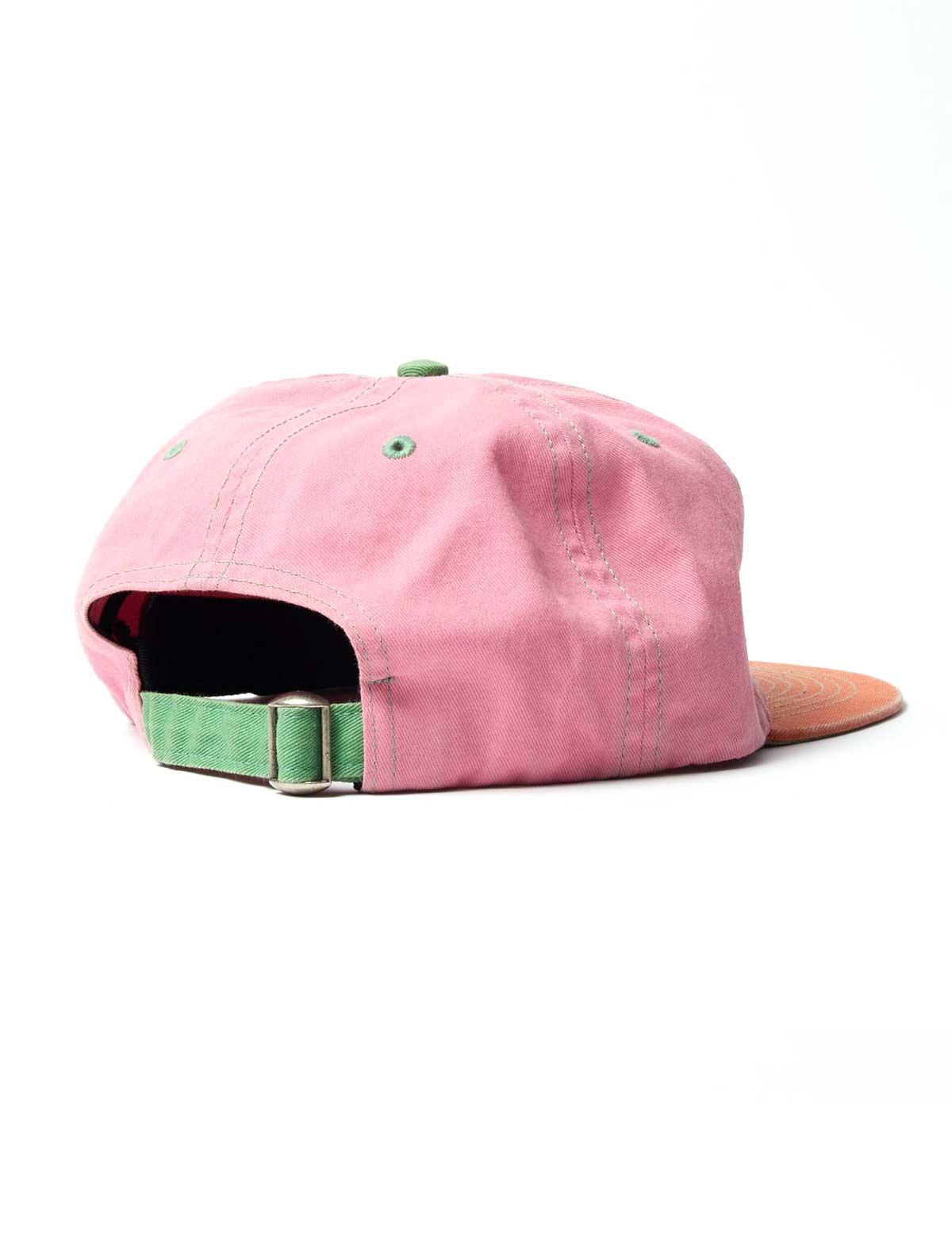 A pink cotton baseball cap shown from a rear three-quarter angle, featuring a green adjustable strap with a metal buckle, a green button on top, and a brown leather visor.