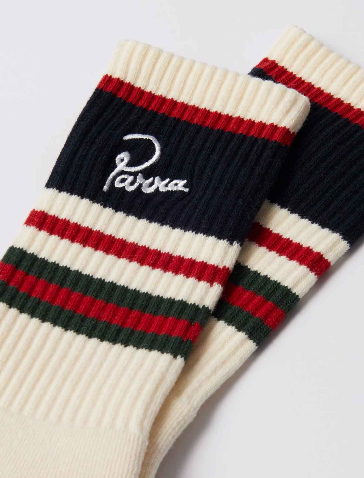 A pair of ribbed knit crew socks in cream, navy, red, and green stripes, with the brand name 'Parra' embroidered in white script on the navy section.