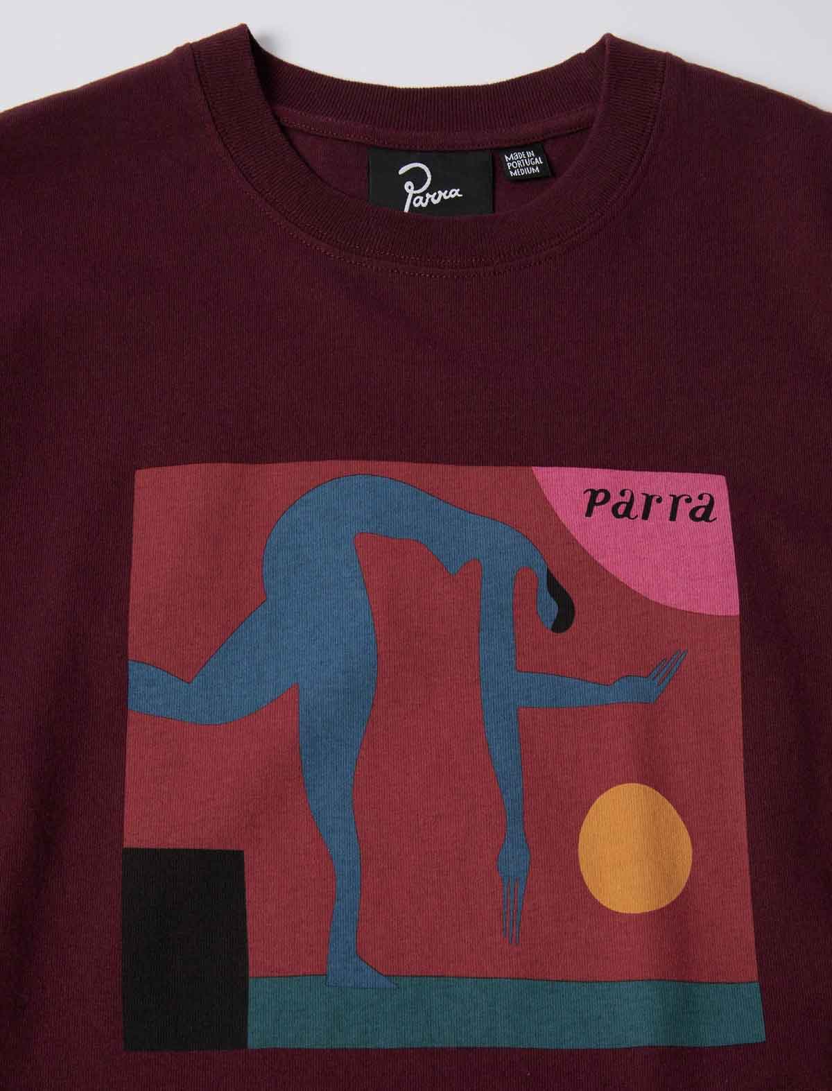 A close-up of a maroon crewneck sweatshirt featuring a large graphic print on the front. The graphic depicts a blue stylized figure in a geometric scene with a pink sun, yellow circle, and black block, with the word 'Parra' printed in black.