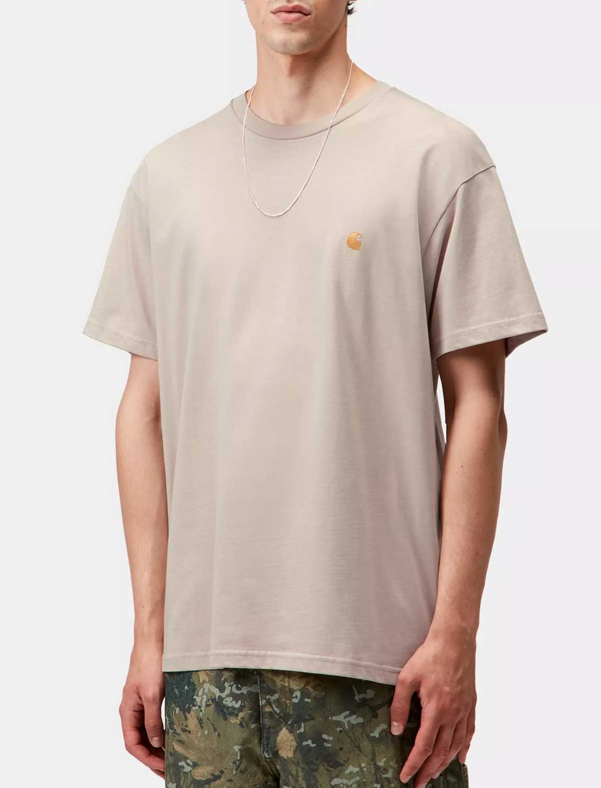 Person wearing a carhartt wip chase beige t-shirt with a small logo on a white background