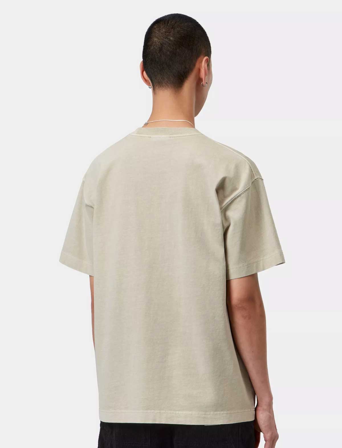 A man viewed from behind wearing an oversized light beige t-shirt and black pants, photographed against a clean white studio background.