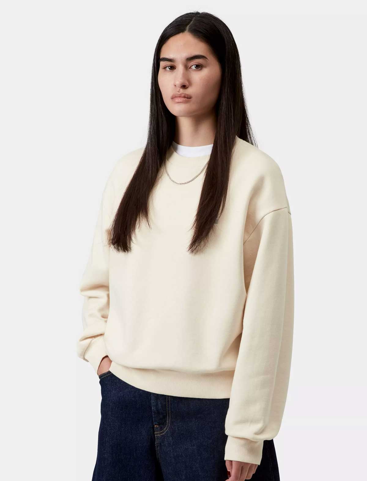 Person wearing a cream sweatshirt and dark pants on a white background