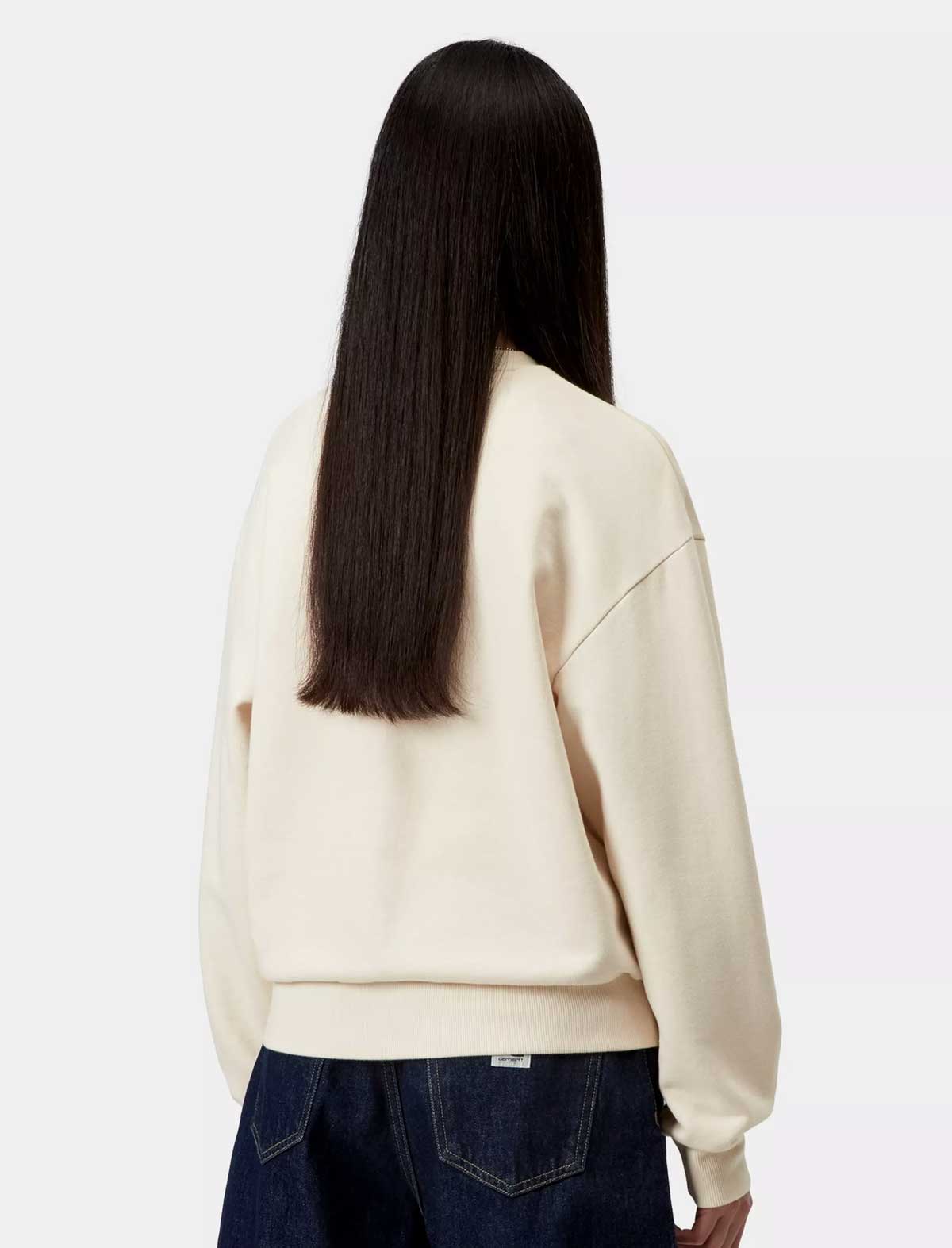 Person wearing a beige sweatshirt and dark jeans on a white background