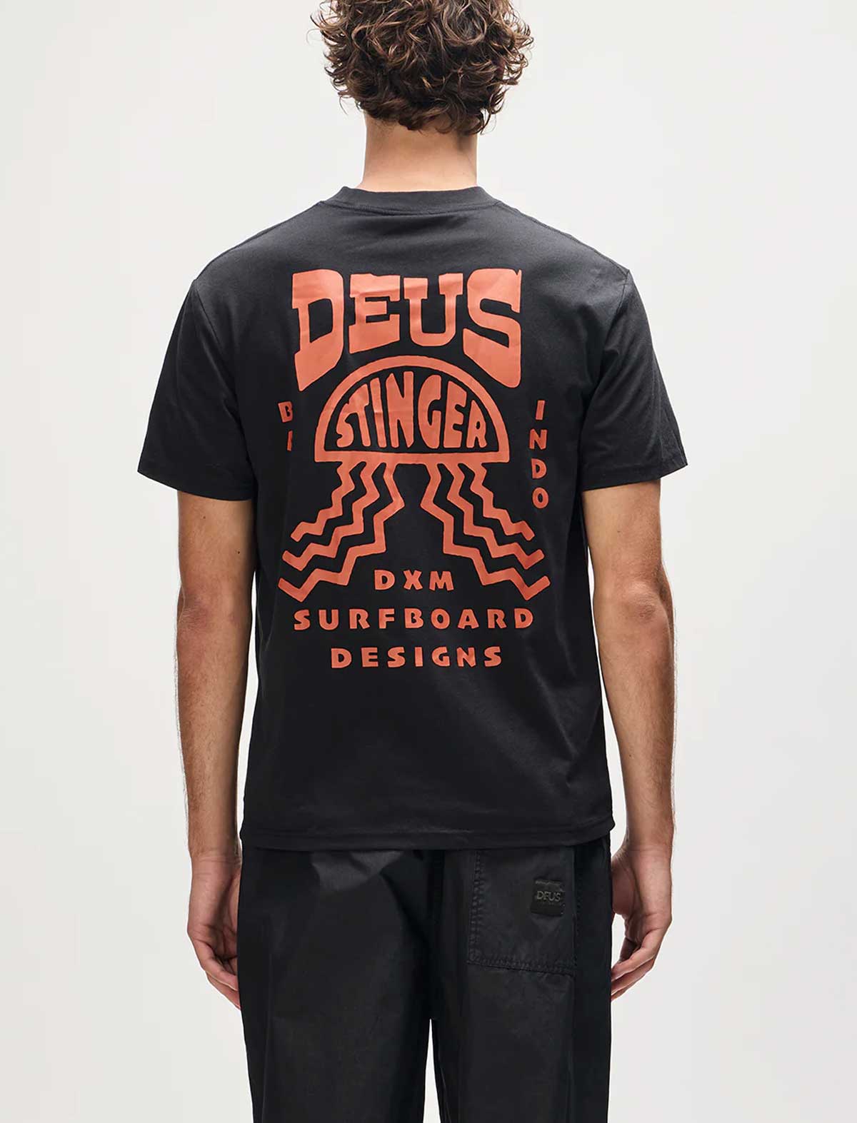 Person wearing a black t-shirt with orange graphics and text on the back, on a plain background