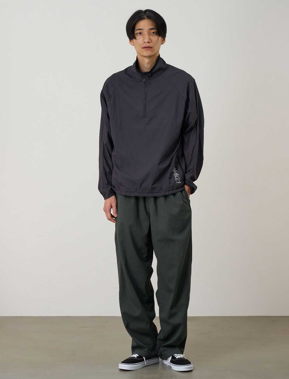 Person wearing a dark jacket and pants against a plain background