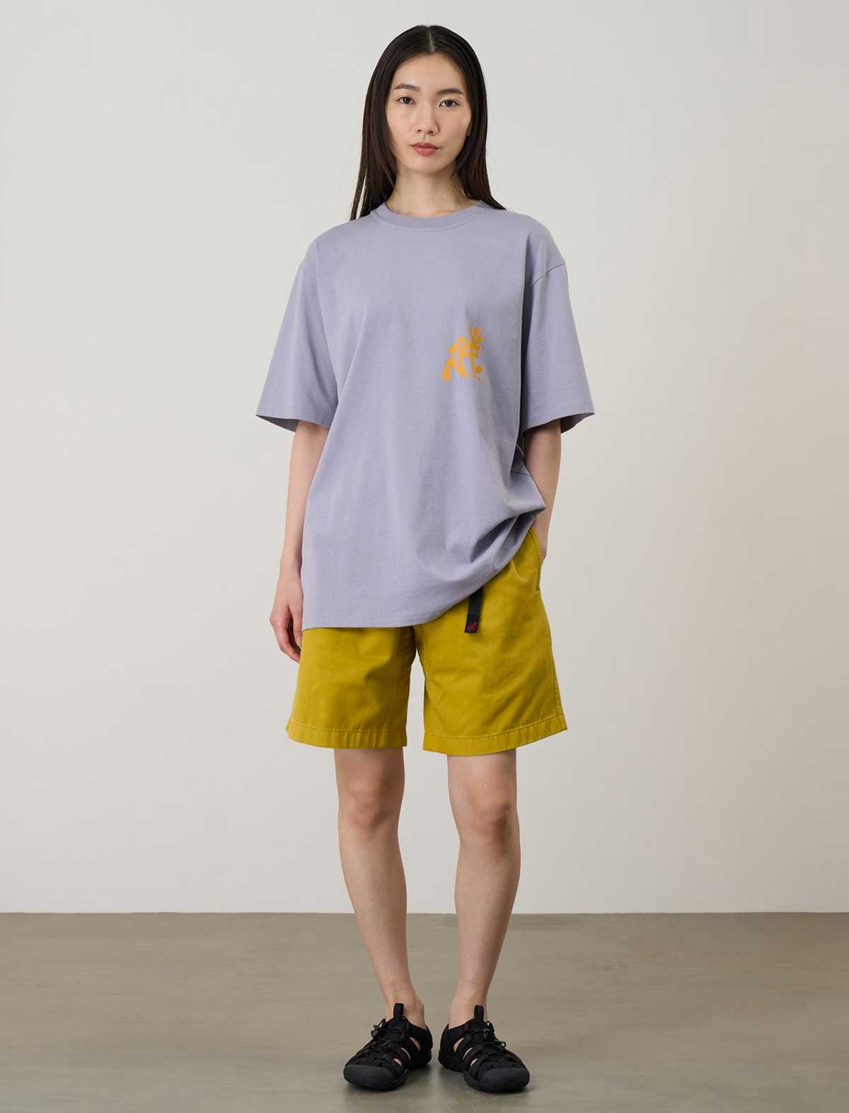 Person wearing a Gramicci light purple t-shirt with a yellow logo and yellow shorts against a plain background