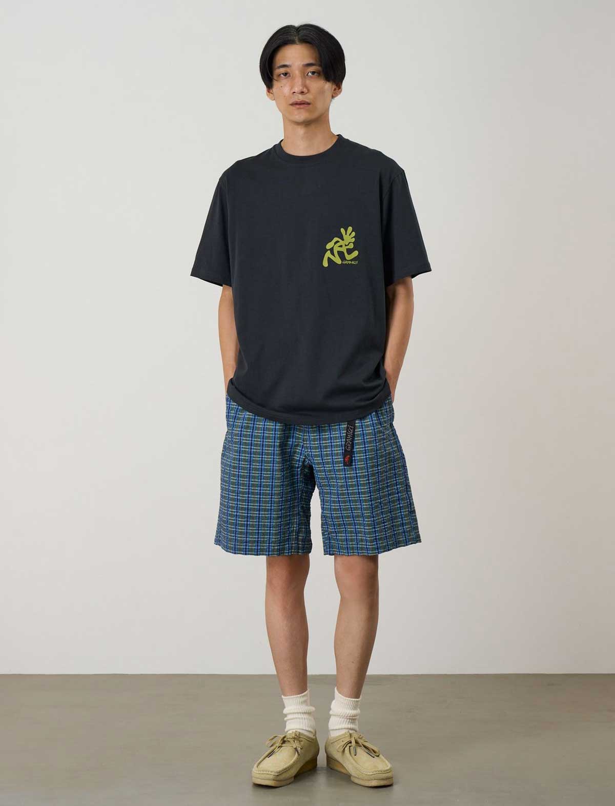 Person wearing a black t-shirt with a yellow graphic and blue plaid shorts against a plain background