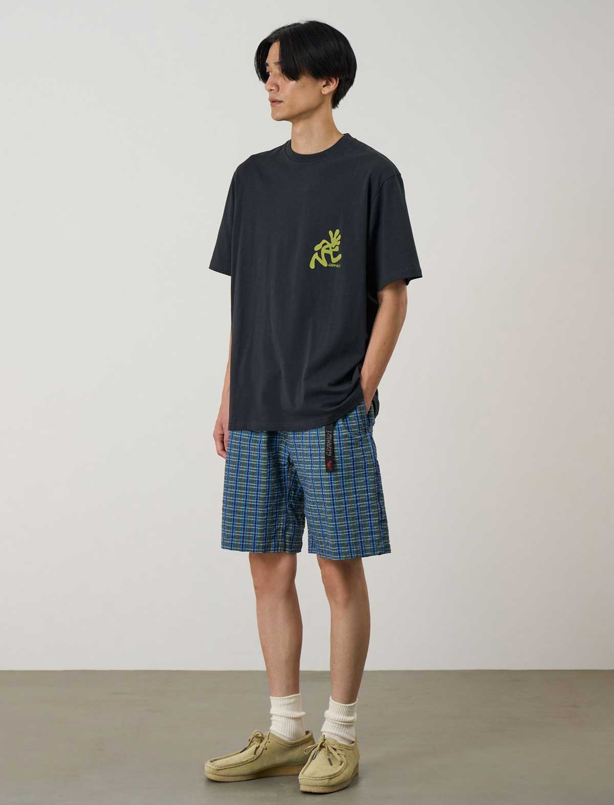 Person wearing a black t-shirt with a logo and plaid shorts against a plain background