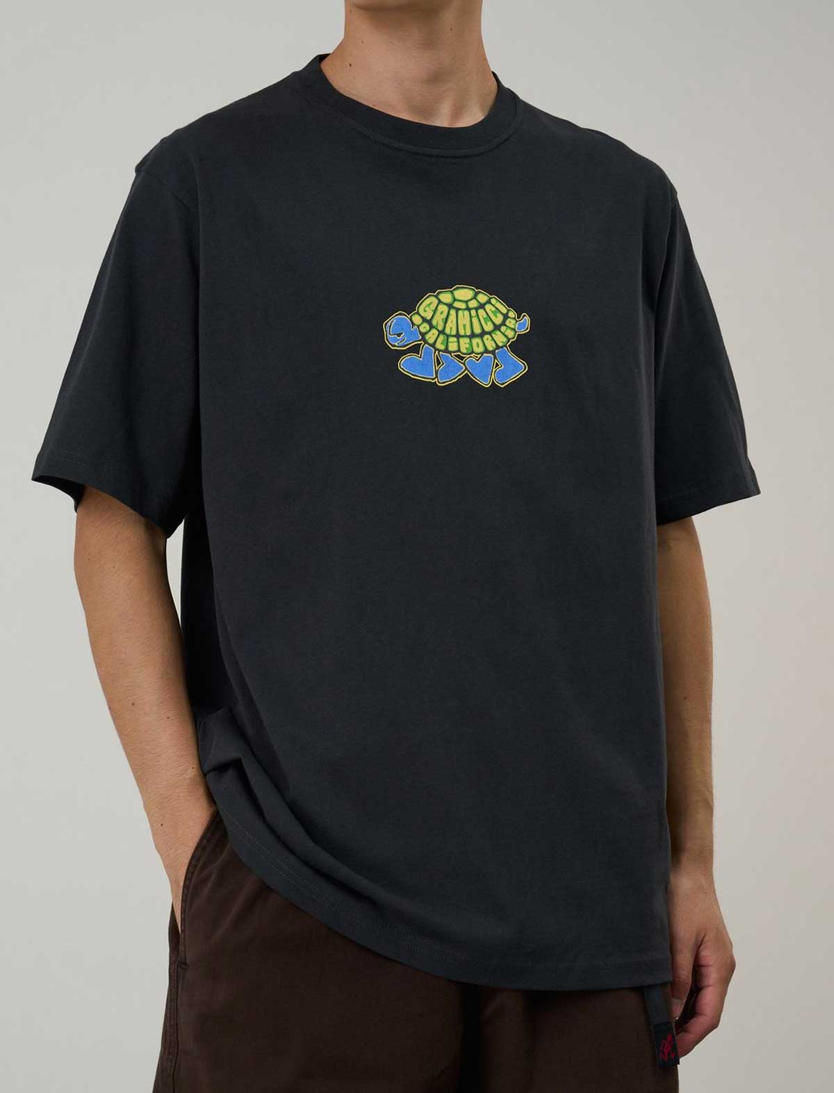 Person wearing a Gramicci black t-shirt with a turtle graphic on a plain background