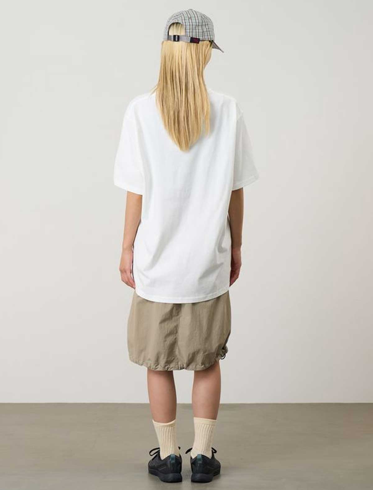 Person wearing a white t-shirt, beige shorts, and a cap from behind on a plain background