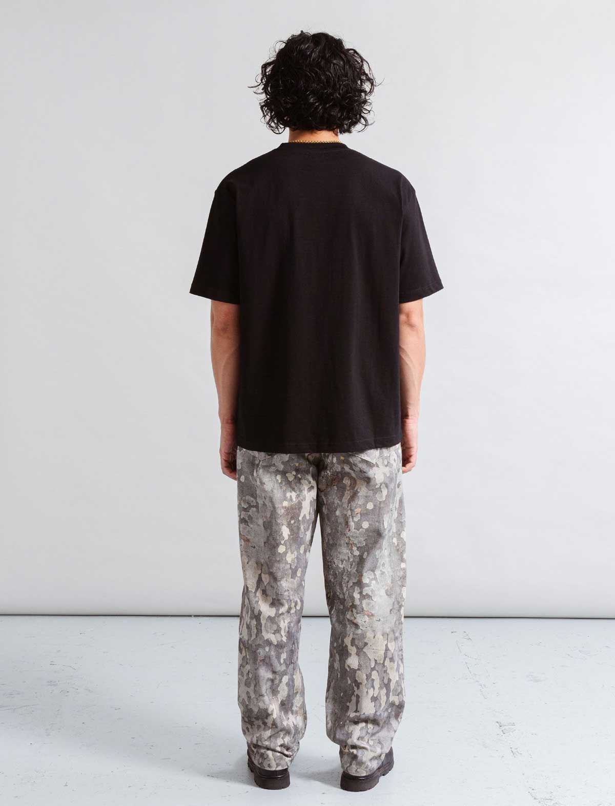 Person wearing a black t-shirt and camouflage pants standing against a plain white background