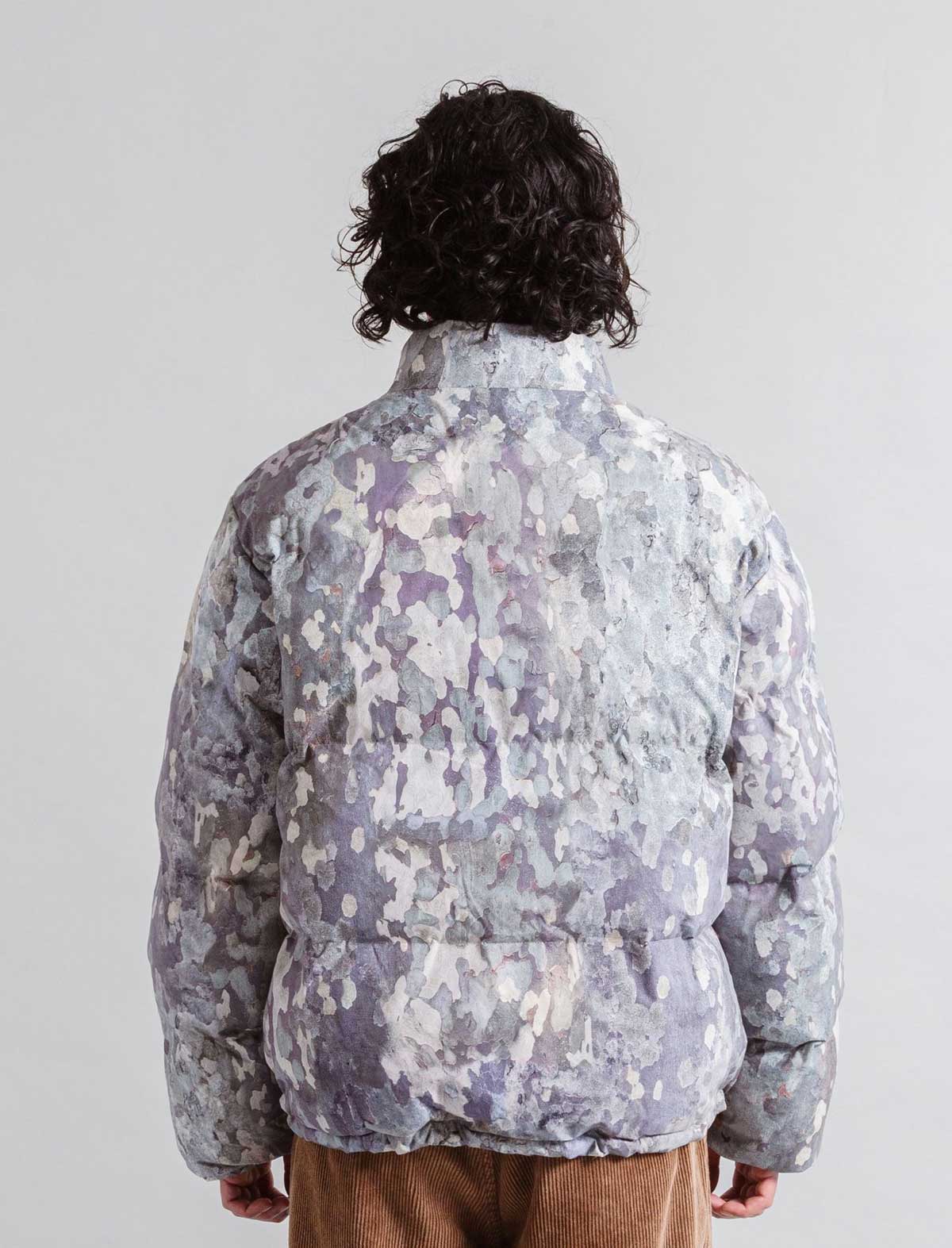 Person wearing a Heresy camouflage jacket from behind on a plain background