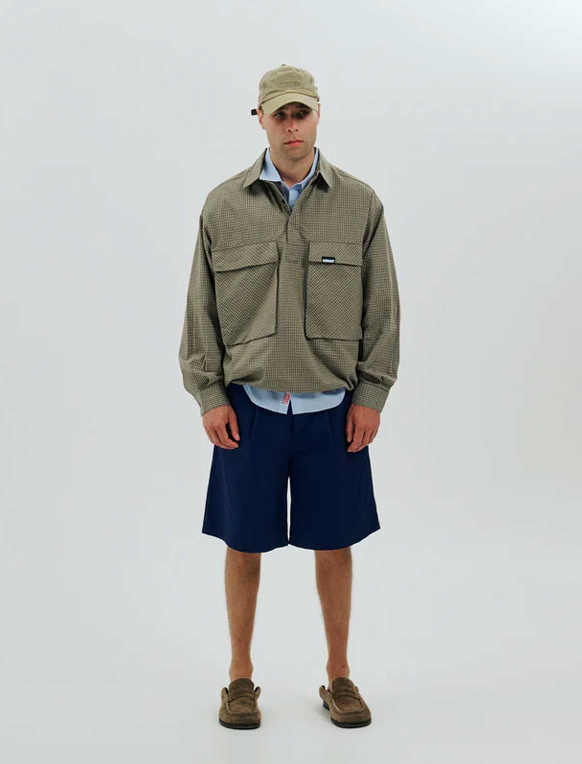 Person wearing a green jacket, blue shorts, and a cap on a white background