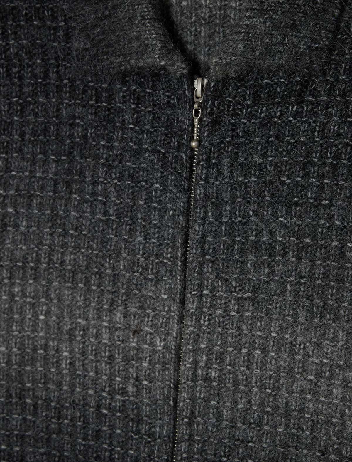 Close-up of a dark charcoal gray textured zip-up jacket with a fine waffle or tweed-like weave and a central zipper.