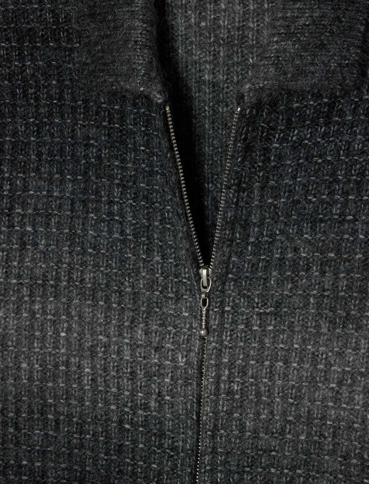 Close-up of a dark charcoal gray waffle-knit zip-up garment with a silver zipper running down the center.