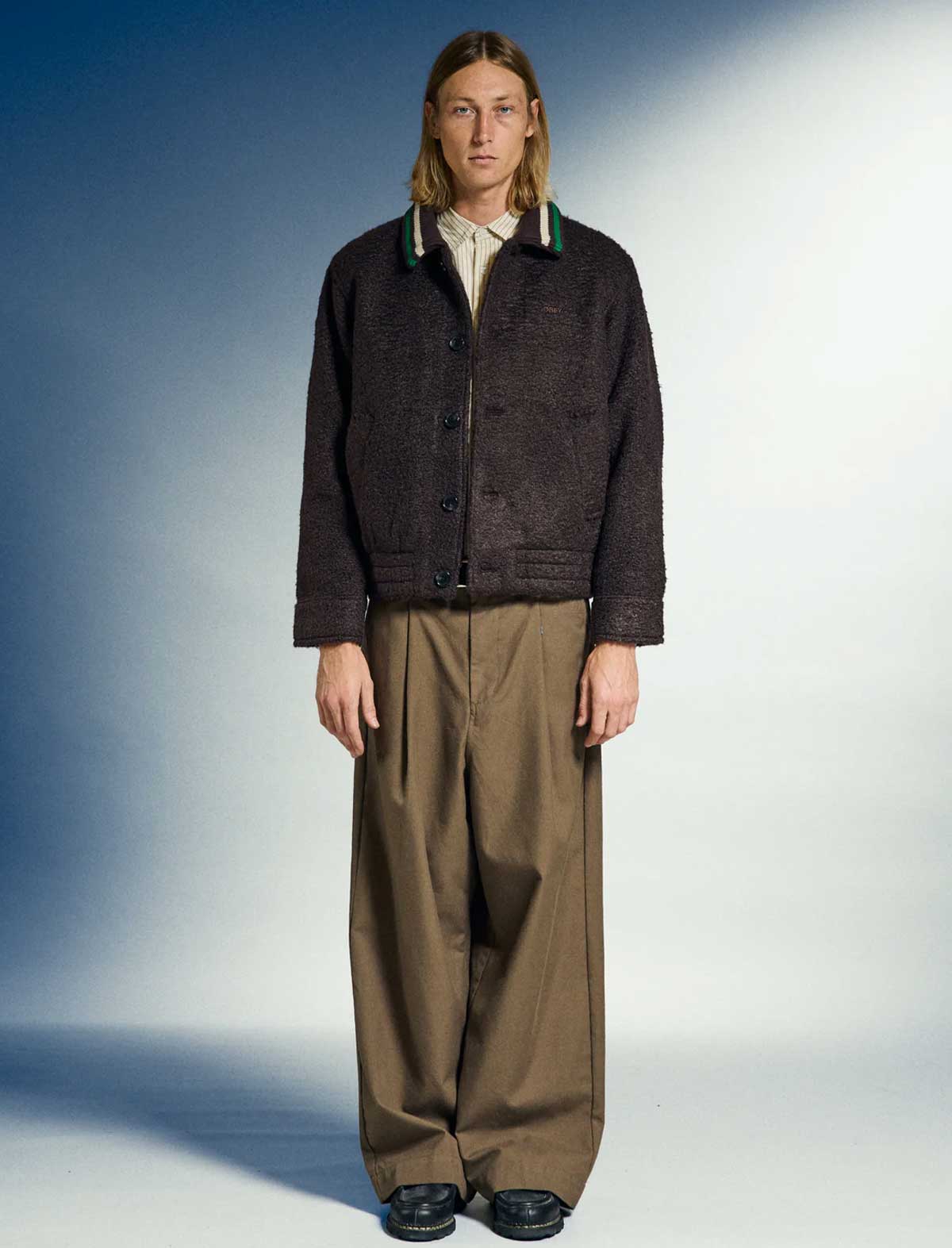 Person wearing a dark jacket and brown pants against a gradient background