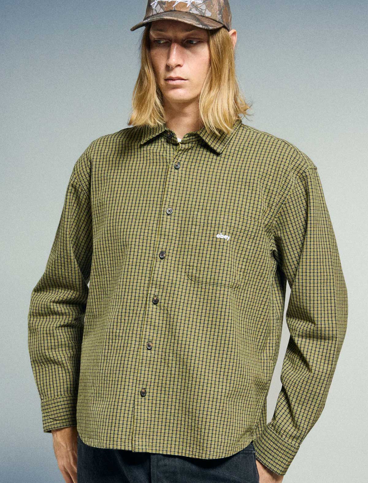 Person wearing a green checkered shirt with a logo on a gray background