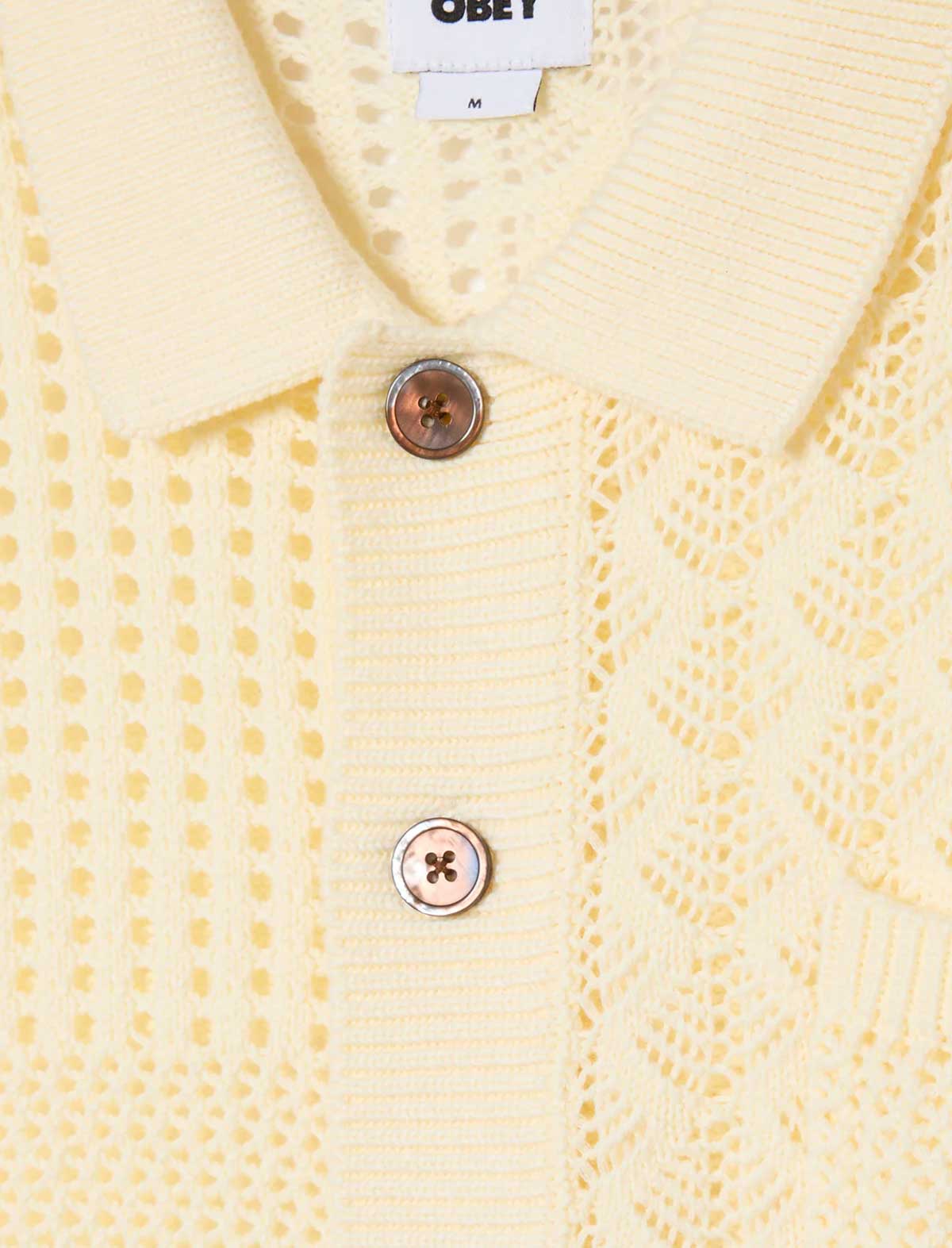 Close-up of a yellow textured cardigan with buttons and 'Obey' brand tag.