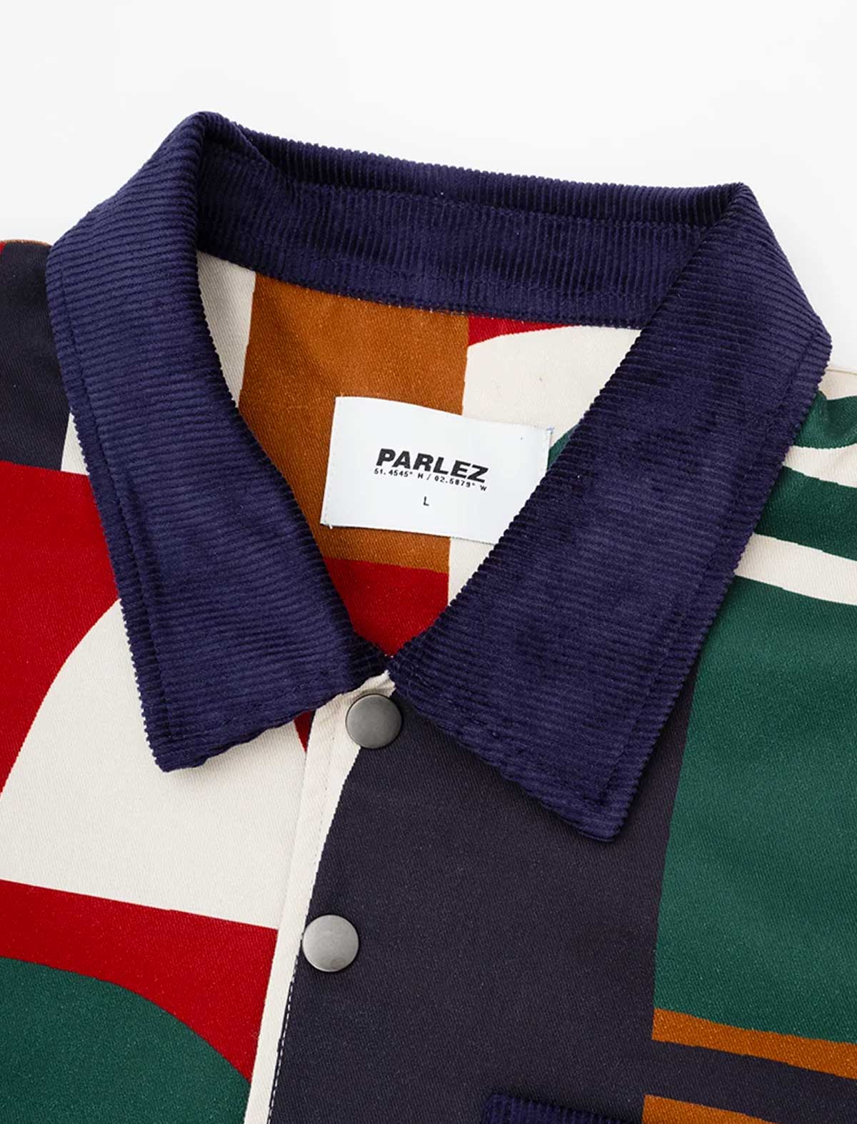 Close-up of the Parlez Bolt Jacket in Multi's navy corduroy spread collar and woven orange Parlez branded neck tag, against the geometric print body fabric.