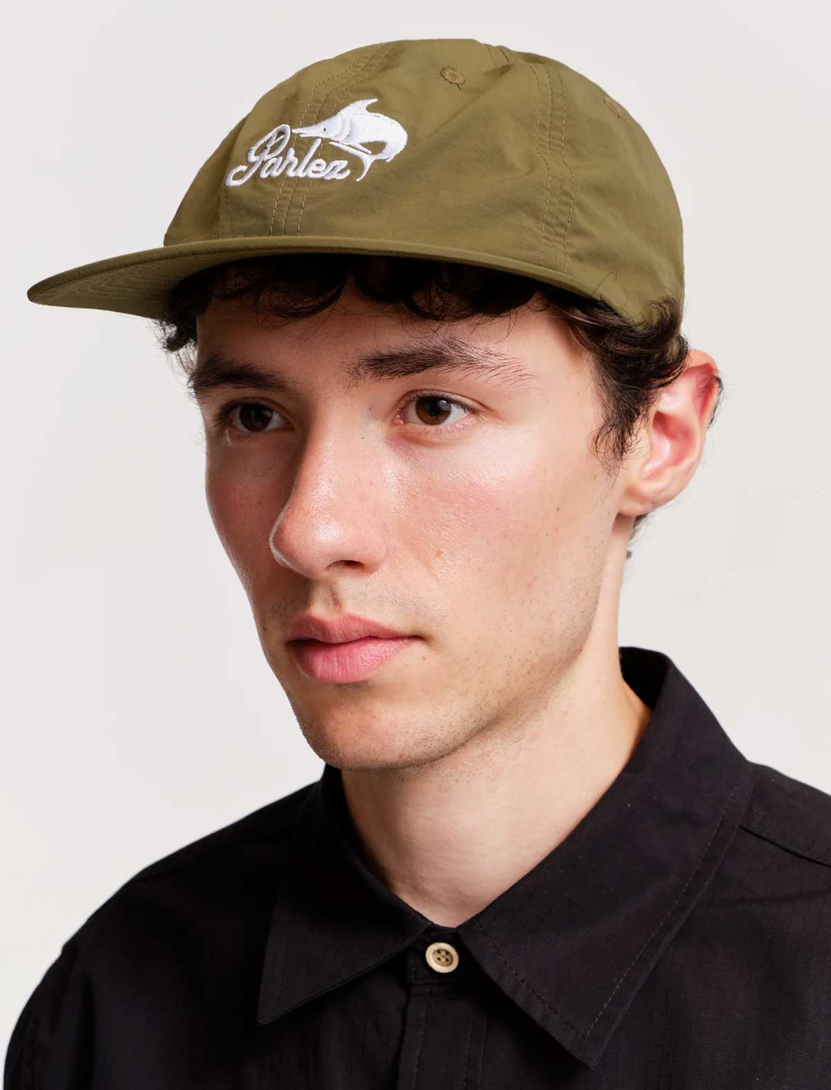 Man wearing a green cap with a logo on a plain background