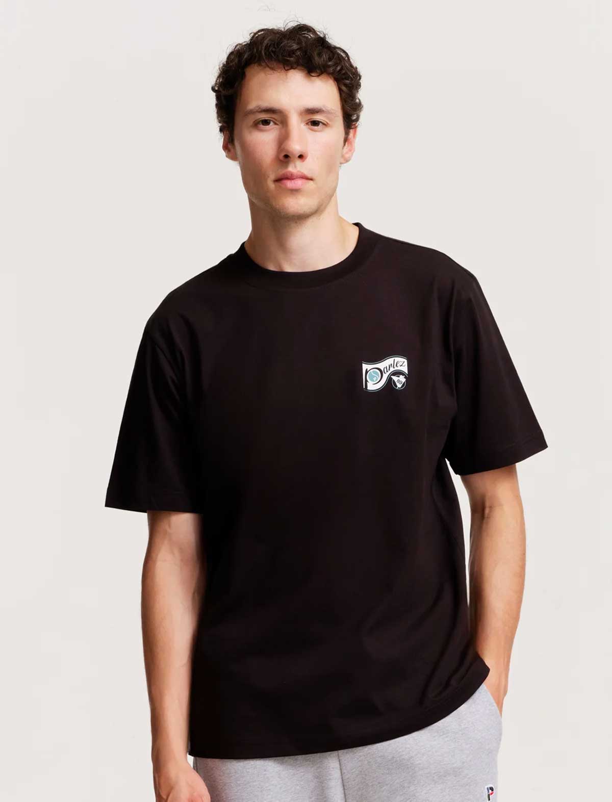Person wearing a parlez ludis black t-shirt with a small logo on a plain background 