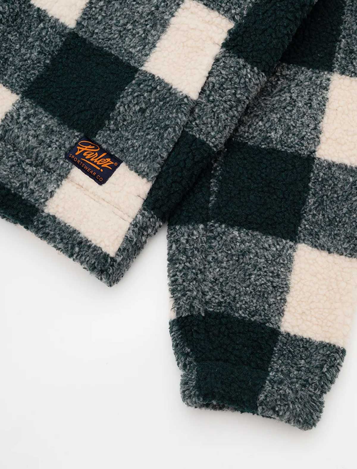 Close-up of the Parlez Province Check Sherpa Fleece Jacket in Deep Green's cuff, showing the green and cream buffalo check sherpa fleece with a woven orange Parlez branded tab.