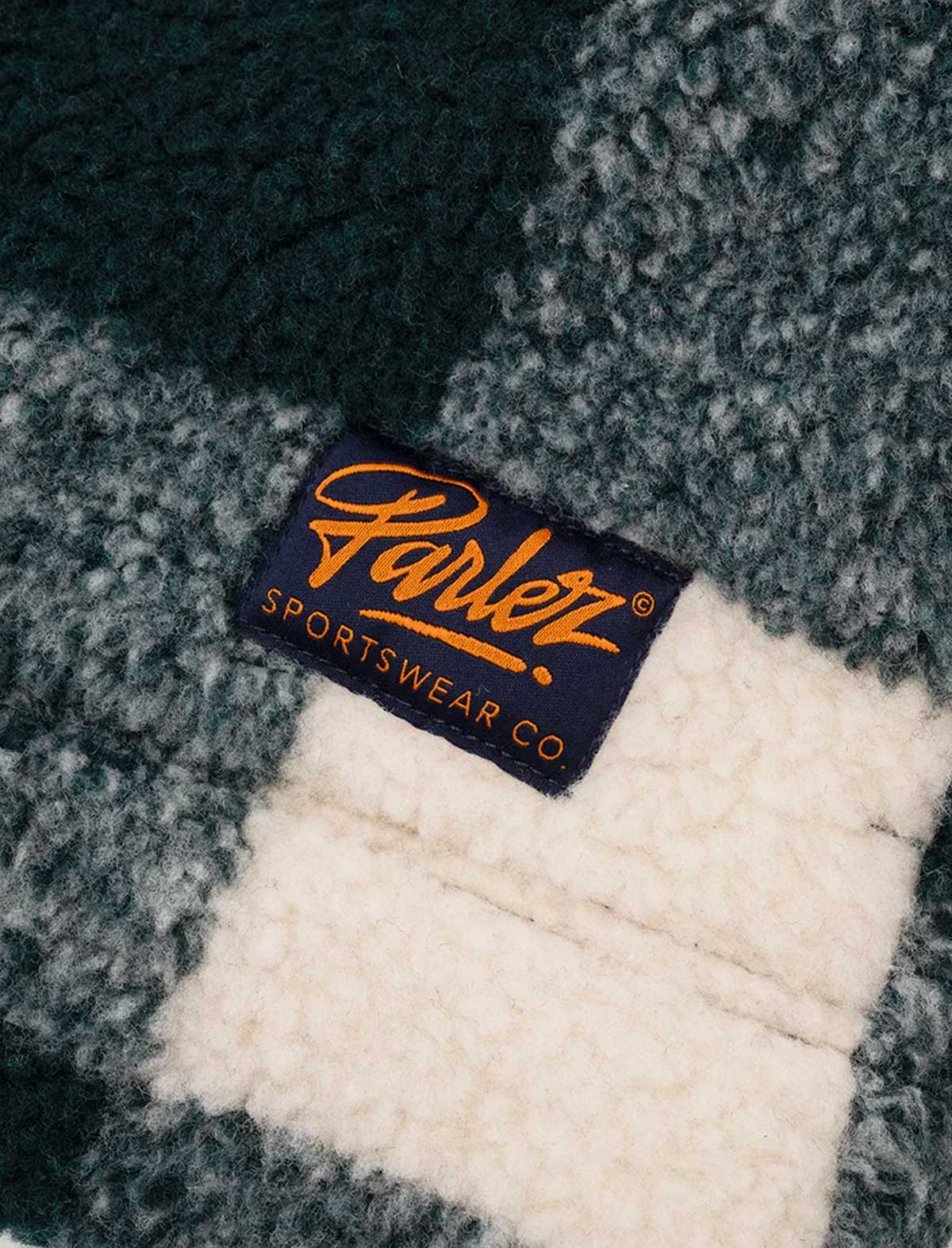 Close-up of the Parlez Province Check Sherpa Fleece Jacket in Deep Green's grey high-pile sherpa fleece texture with a woven navy Parlez script logo patch.
