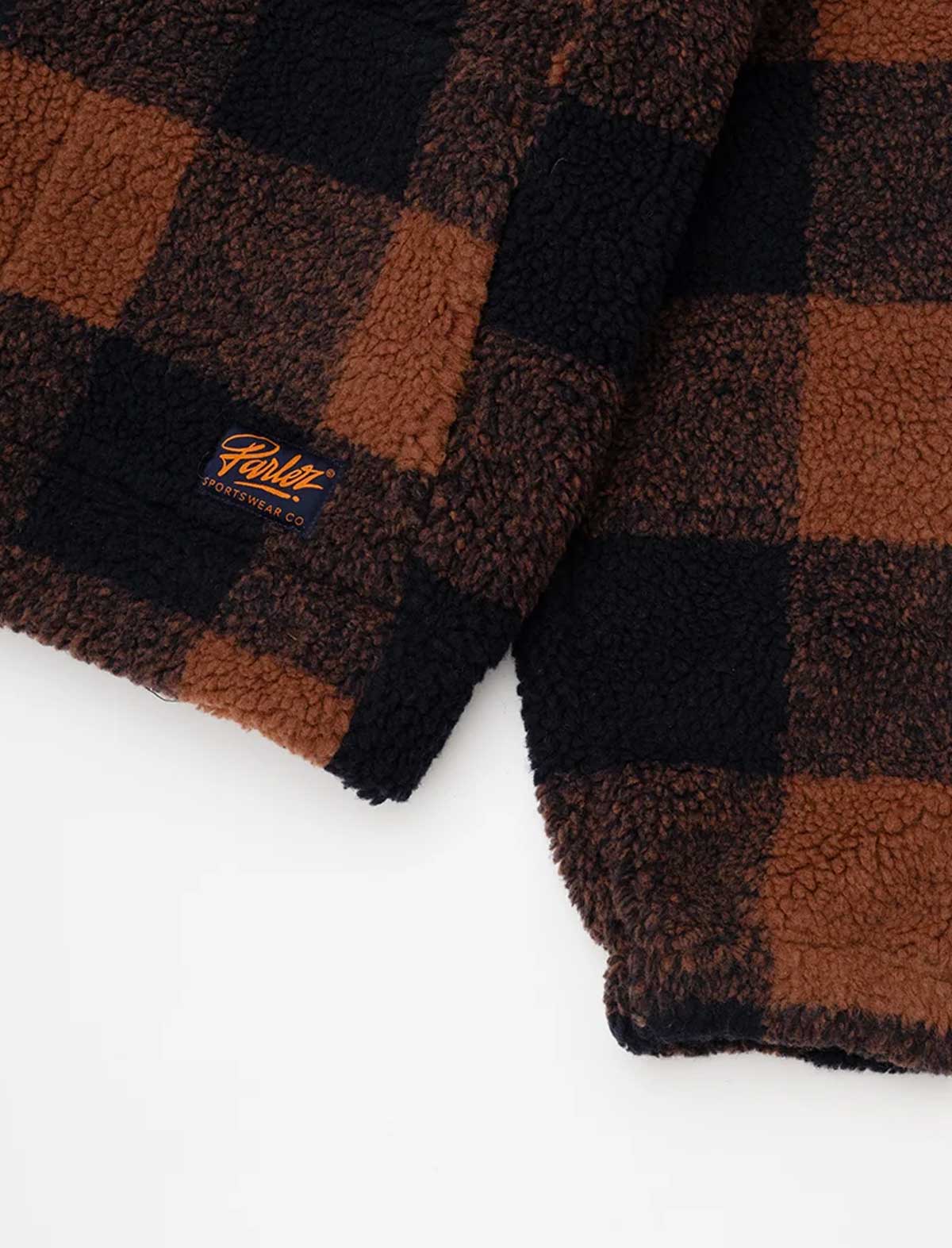 Close-up of a brown and black buffalo plaid sherpa fleece garment, showing the textured fleece fabric and a small embroidered Parley New York logo patch.