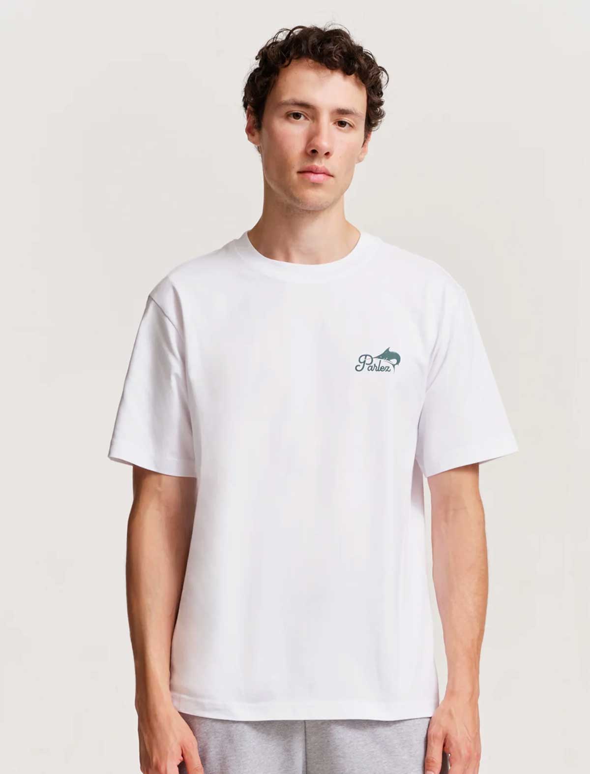 Person wearing a white parlez release t-shirt with a small logo on a plain background