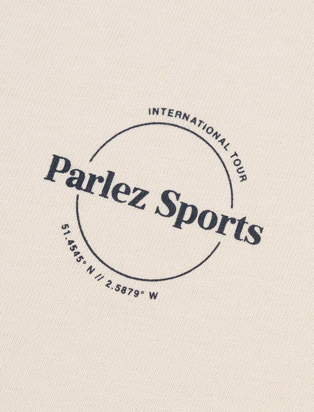 Close-up of a light beige fabric surface with a dark navy circular logo reading 'Parlez Sports' and smaller text 'International Tour' and coordinates.