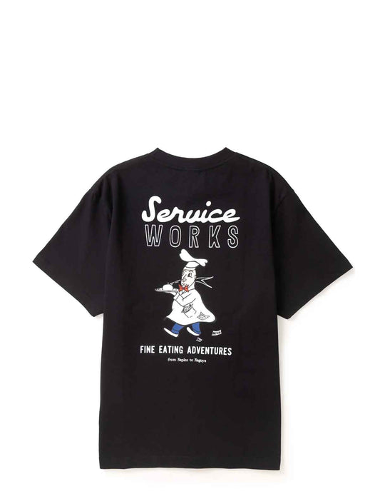 A black short-sleeve t-shirt with a graphic print on the back. The print features the words 'Service Works' in white script and block letters, a cartoon chef character in a white uniform, and 'FINE EATING ADVENTURES' in white text below.